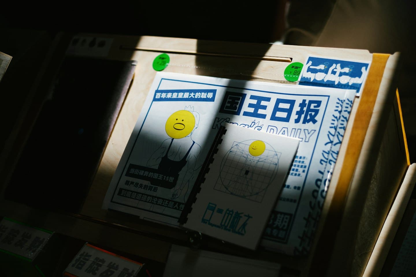 Two satirical newspapers with smiley face graphics on a wooden stand.